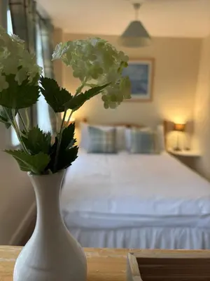 a white vase with flowers on a table with a bed at The Harp Inn in Old Radnor