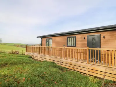 a wooden house with a wooden fence in a field at Seren Lodge in Builth Wells