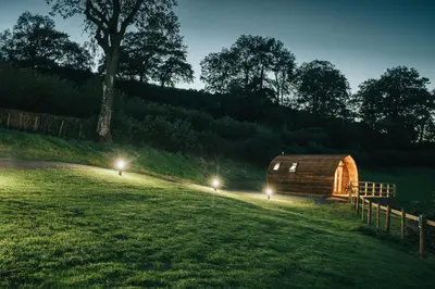 a wooden barn with lights in a field at night at Knighton by Wigwam Holidays in Knighton