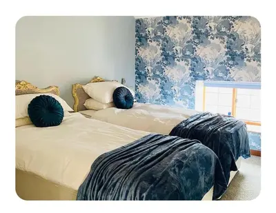 two beds in a bedroom with blue floral wallpaper at The Coach House in Berriew