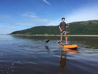 a man standing on an orange paddle board in the water at Glannant - 5 Bed & 4 Bathroom - Fairbourne, Barmouth, Mawddach Estuary in Arthog