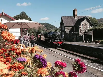 a train pulling into a train station with flowers at Station House - Hw7742 in Glyn-Dyfrdwy