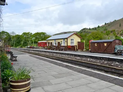 a train station with a building and a bench next to the tracks at Station House - Hw7742 in Glyn-Dyfrdwy