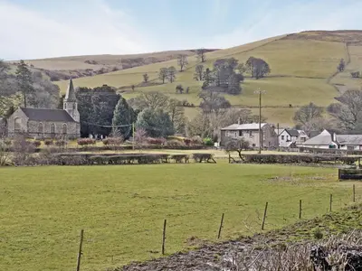 a village with a field and a church and hills at The Coach House - Hw7782 in Llanarmon Dyffryn-Ceiriog