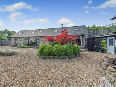 a stone house with a red bush in front of it at West Barn in Llansadwrn