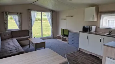 a kitchen and living room with a couch and a tv at Lyons Sunnysands Caravan Park in Barmouth