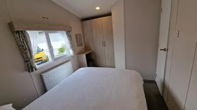 a small bedroom with a white bed and a window at Lyons Sunnysands Caravan Park in Barmouth
