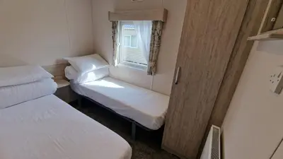 a small room with two beds and a window at Lyons Sunnysands Caravan Park in Barmouth