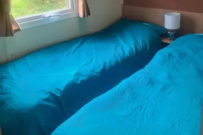 a bedroom with two blue pillows and a window at 3 Bed Caravan - Sleeps 6 - Pets - Parking - Wifi in Borth
