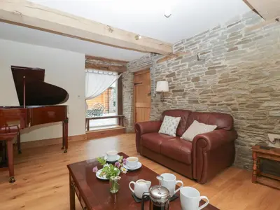 a living room with a leather couch and a piano at Evenjobb Court Farmhouse in Presteigne