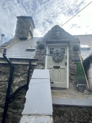 a stone house with a white door and a stone wall at Top Cottage Barmouth in Barmouth