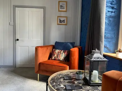 a living room with an orange chair and a glass table at Secluded farmhouse with views in Cwrt-newydd