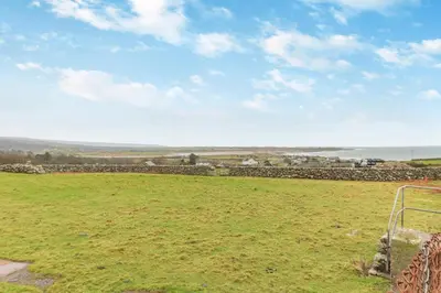 a grassy field with a stone wall and the ocean at 2 Bed in Llanfair oc-a30451 in Llanfair
