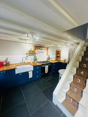 a kitchen with blue cabinets and a sink and stairs at Little Cottage, Llwyngwril in Llwyngwril