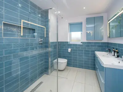 a blue tiled bathroom with a toilet and a sink at Modern 4-Bed Home Spacious & Comfortable - Pass the Keys in Pontesbury