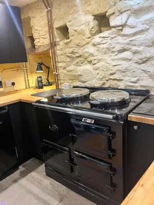 a kitchen with a stove with a stone wall at Glovers cottage private hot tub and super king in Llanrhystyd