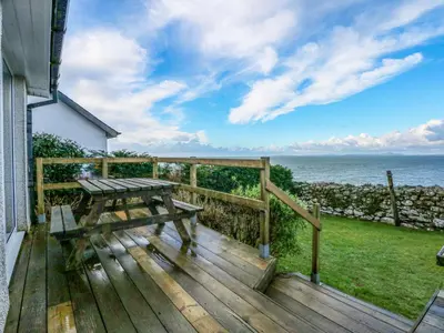 a wooden deck with a picnic table and the ocean at Ael Y Don in Harlech