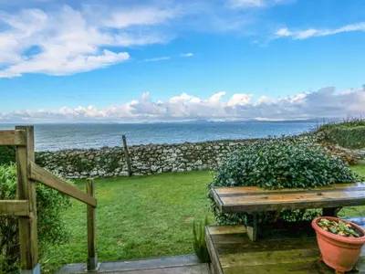 a wooden picnic table with a view of the ocean at Ael Y Don in Harlech