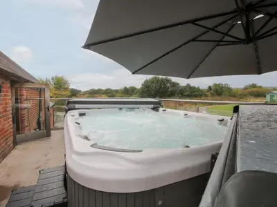 a hot tub with an umbrella on a patio at Millstone Cottages - Breidden View in Shrewsbury
