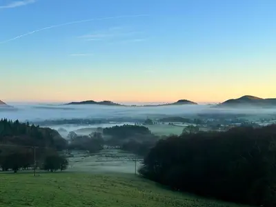 a foggy valley in the hills with trees and mountains at Carol Anns Caravan, Working Farm Stay, Rural, Private, Fire Pit for hire, Dogs on request in Pontesbury