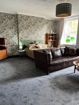 a living room with a leather couch and floral wallpaper at Large Corris apartment with kitchen & lounge and adjoining bathroom in Dolgellau