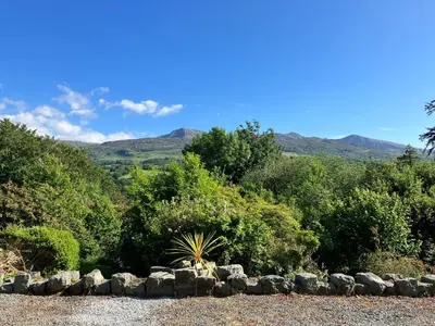 a garden with rocks and trees with mountains in the background at Large Corris apartment with kitchen & lounge and adjoining bathroom in Dolgellau