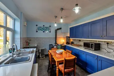 a kitchen with blue cabinets and a wooden table at Finest Retreats - Tan y Fron Hideaway in Dyffryn