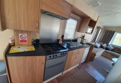 a small kitchen with a stove and a living room at Pet Friendly 3 Bed Static Caravan in Clarach Bay Spacious and Cozy Stay in Aberystwyth