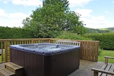 a hot tub on a wooden deck with a bench at Bevan House with Hot Tub in Mid-Wales in Hundred House