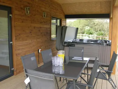 a table and chairs on a porch with a refrigerator at Woodland Lodge Hot Tub Sleeps 6 in Hundred House