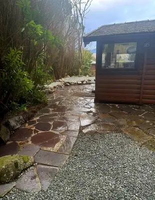 a stone walkway next to a house with a building at Misty Mountain Log Cabin - Trawsfynydd in Trawsfynydd