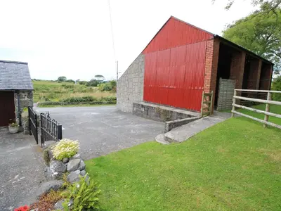 a red barn with a fence next to a parking lot at Y Stabl The Old Stable in Llanbedr