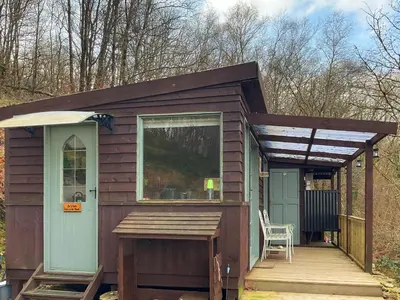 a tiny house with a porch and a chair on a deck at The Cabin In The Woods - Uk49023 in Pencarreg