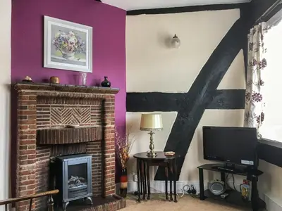 a living room with a brick fireplace and purple walls at The Cottage in Weobley