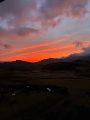 a sunset in a field with mountains in the background at Beautiful Remote Cottage near Dolgellau in Penmaen Pool