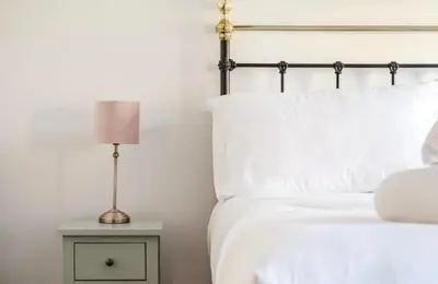 a white bed with a lamp on a night stand at Bramble Cottage in Atcham