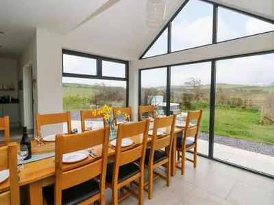 a dining room with a table and chairs and large windows at Rhandir Hen in Aberystwyth