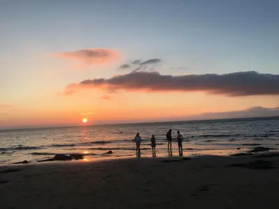 three people standing on the beach watching the sunset at POD2 Family Glamping with seaview & Wi-Fi in Llwyngwril