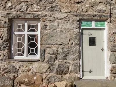 a stone wall with a white door and a window at Clywedog Cottage in Dolgellau