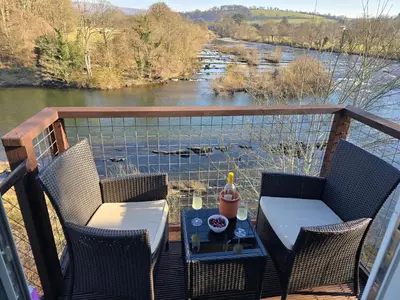a table and chairs on a balcony with a view of a river at The Loft at Box Bridge in Brecon