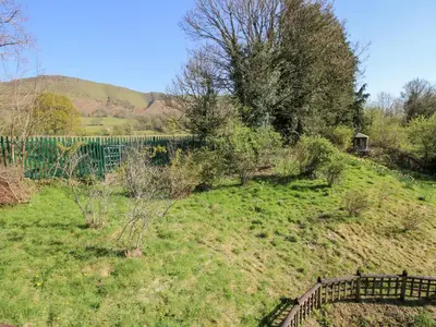 a grassy hill with a fence and a wooden bridge at The Millers Roost at Dudgeley Mill in Church Stretton