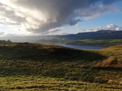 a view of a field with a lake in the distance at Cosy cottage in Snowdonia hamlet in Frongoch