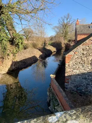 a river with a stone wall next to a canal at The Old Smithy, beautifully restored cottage in Carreghofa, near Llanymynech in Llanymynech