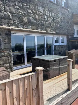 a wooden deck with a stone wall and a table at Bermo Cwtch in Barmouth