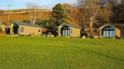 two houses on a grassy field with trees in the background at POD6 Family Glamping with seaview & Wi-Fi in Llwyngwril