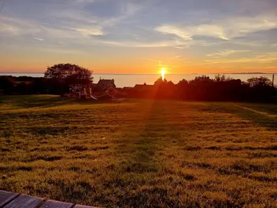 a sunset in a field with the sun setting in the distance at POD6 Family Glamping with seaview & Wi-Fi in Llwyngwril