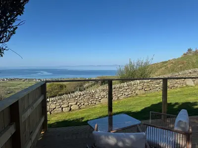 a balcony with chairs and a table and a stone wall at coastal view shepherds hut with hot tub in Llanfair