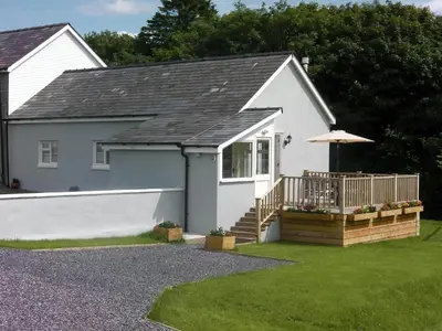 a white house with a deck and an umbrella at Llaethdy Rachel Lampeter in Aberaeron