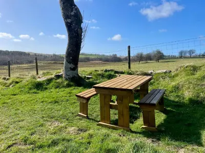 a wooden picnic table and bench in a field at The Viking Lodge with Sauna in Ystrad-Meurig