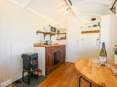 a kitchen with a stove and a table with a bottle of wine at Gilberry Shepherds Hut in Church Stretton